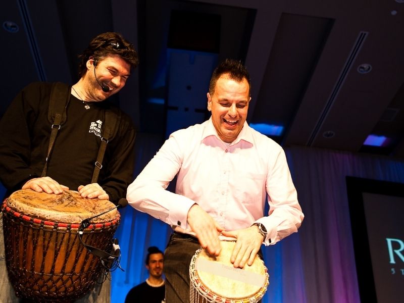 Participants (équipe) jouant des percussions (Djembés) lors d’une activité de team building, souriants et concentrés sur le rythme collectif.